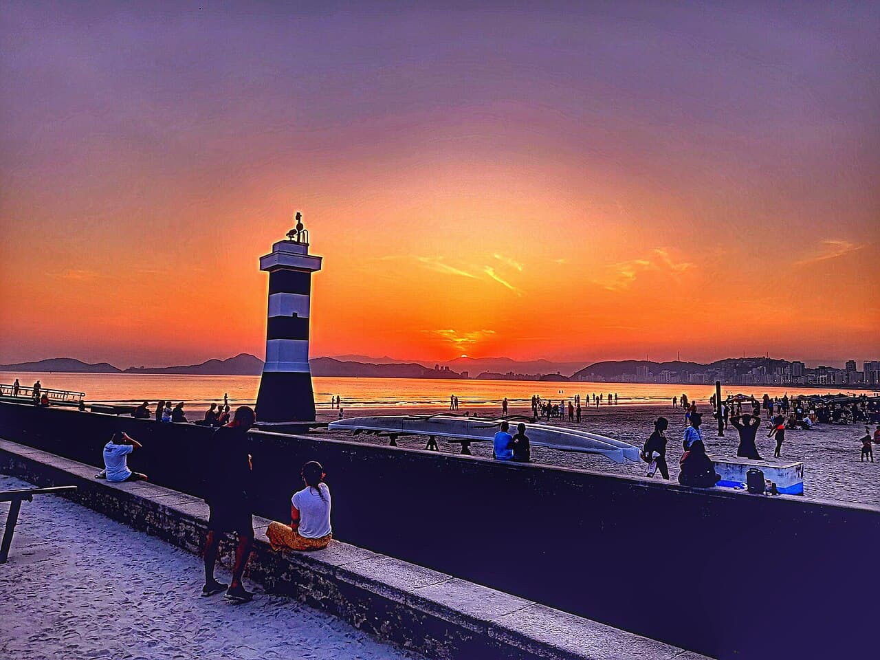 Fim de tarde na orla de Santos, com o farolete no encontro do canal com a praia e os morros ao fundo